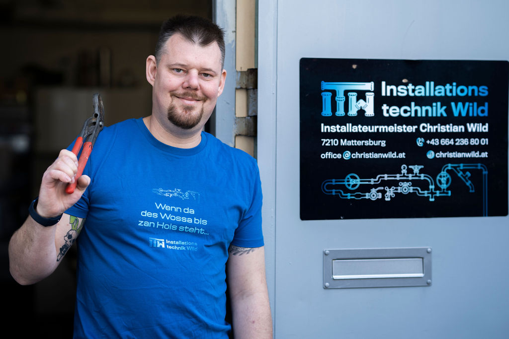 ITW - Portrait von Christian Wild mit Werkzeug in seinen Händen und dem Firmenschild an der Tür